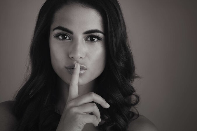 Schwarz-Weiß Portrait einer Frau, die zu Flüstern deutet